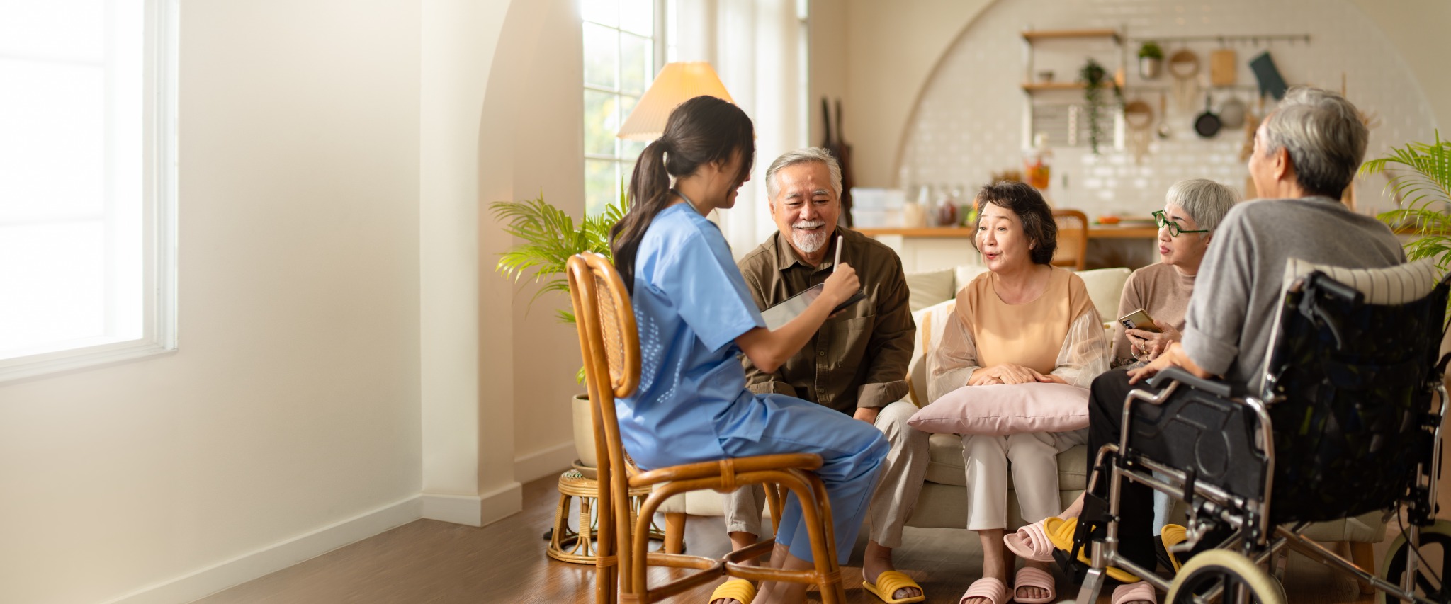 A person in scrubs talking with older adults in a home-like setting.
